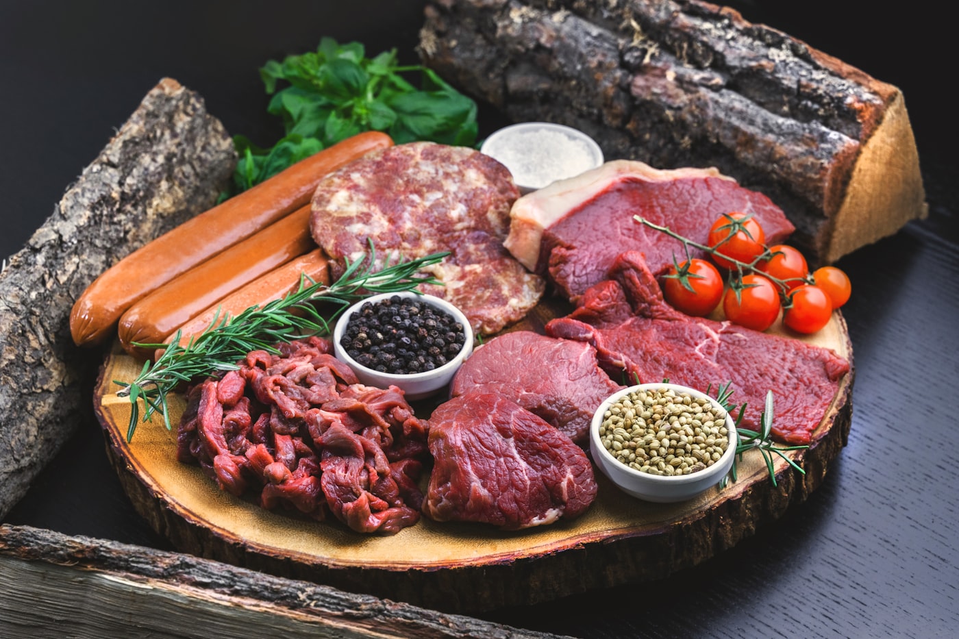 Premium raw meats arranged on a wooden platter with herbs and spices